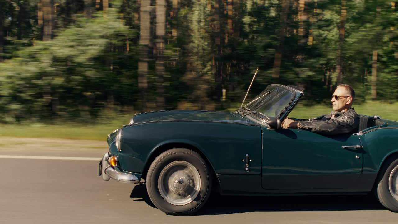 A classic convertible car driving on a road with a man behind the wheel