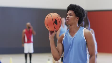 happy african american male basketball player spinning ball on finger at indoor court, slow motion