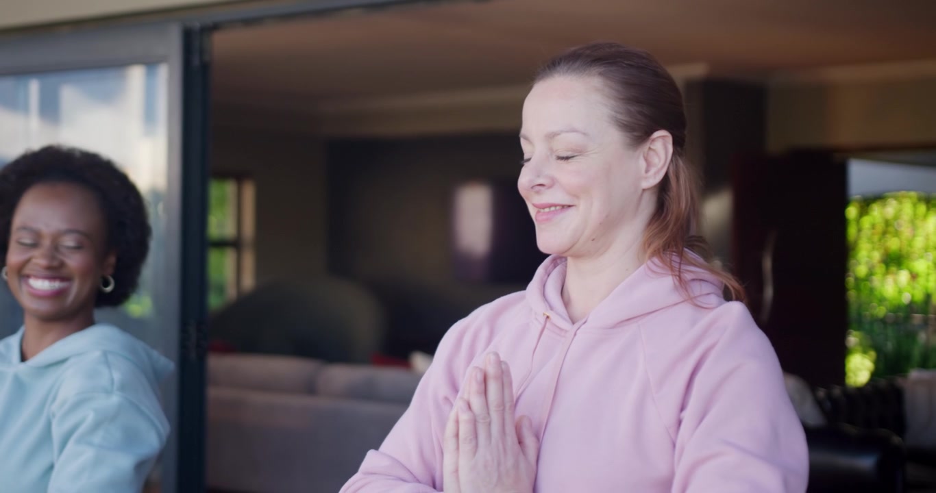 Diverse female friends welcoming other woman entering doorway, one pressing palms, smartwatch