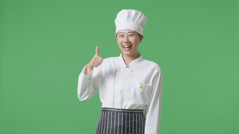 Asian Woman Chef Smiling And Showing Thumbs Up Gesture To Camera While Standing In The Green Screen Background Studio