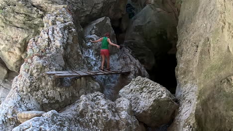 cámara lenta de mujer que cruza un pequeño puente de madera entre rocas