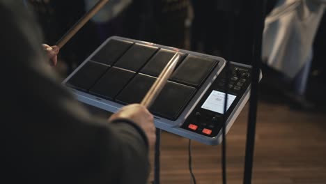 musician playing an electronic drum pad with drumsticks during a live performance