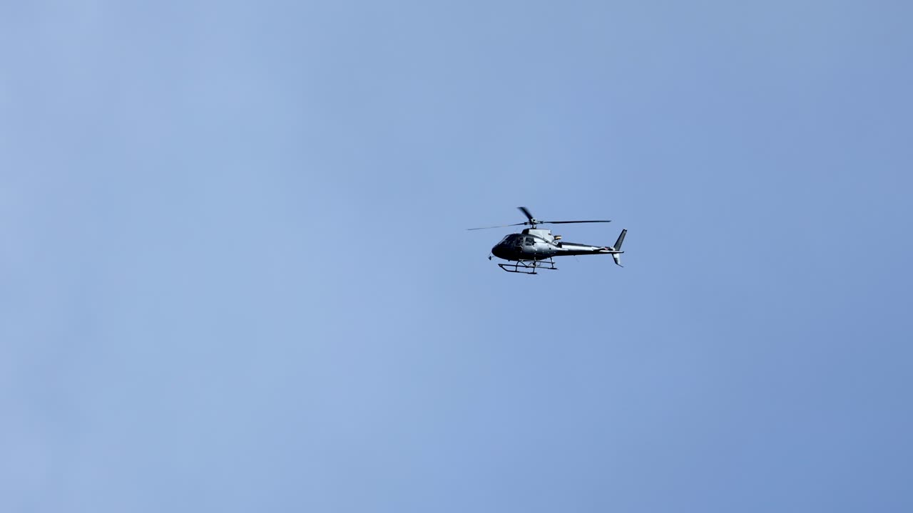 A helicopter flies steadily across a clear blue sky, captured in smooth motion with consistent lighting and serene atmosphere