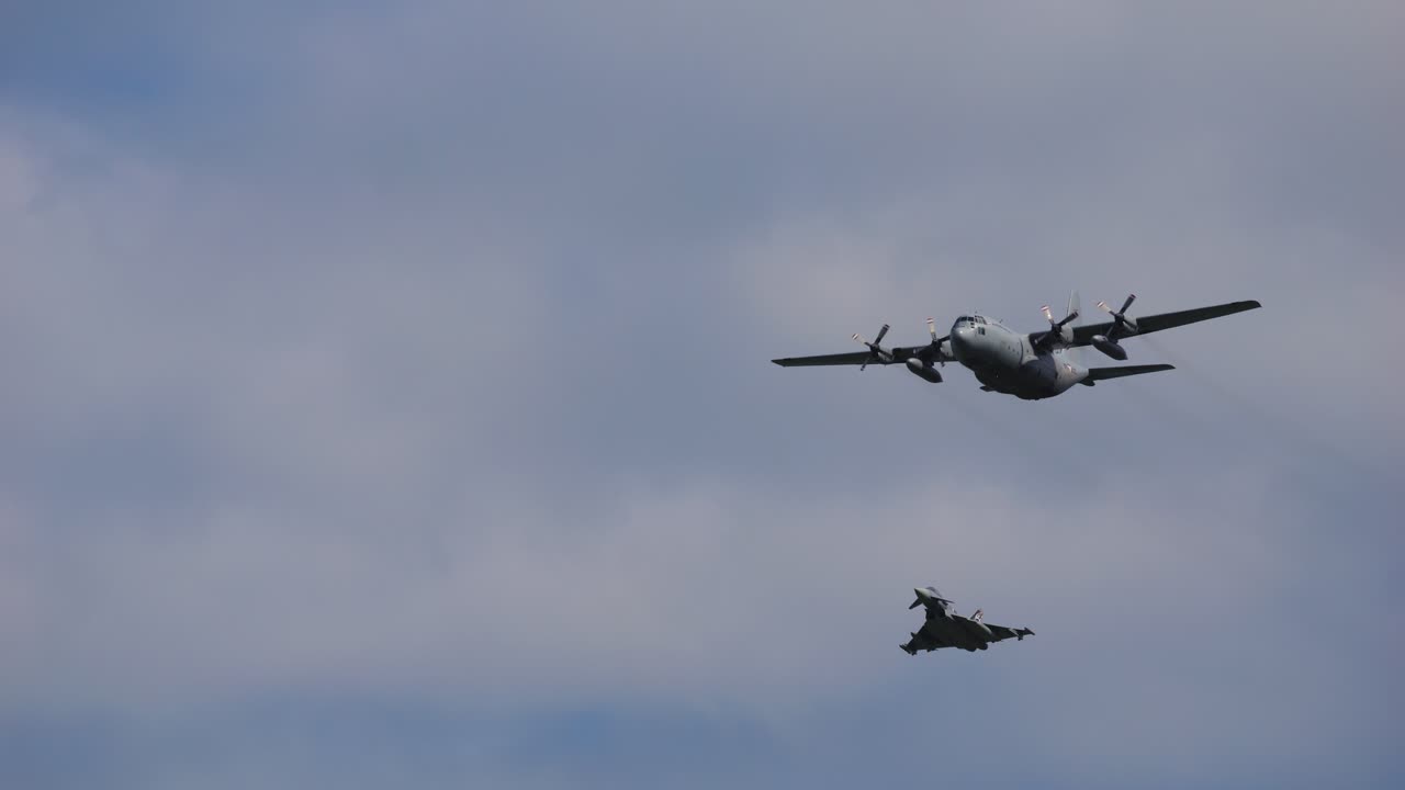 Airplane of the type Airbus A400M and the fighter aircraft types Eurofighter fly through the air with clouds in the background. Taken at the air show called Airpower.