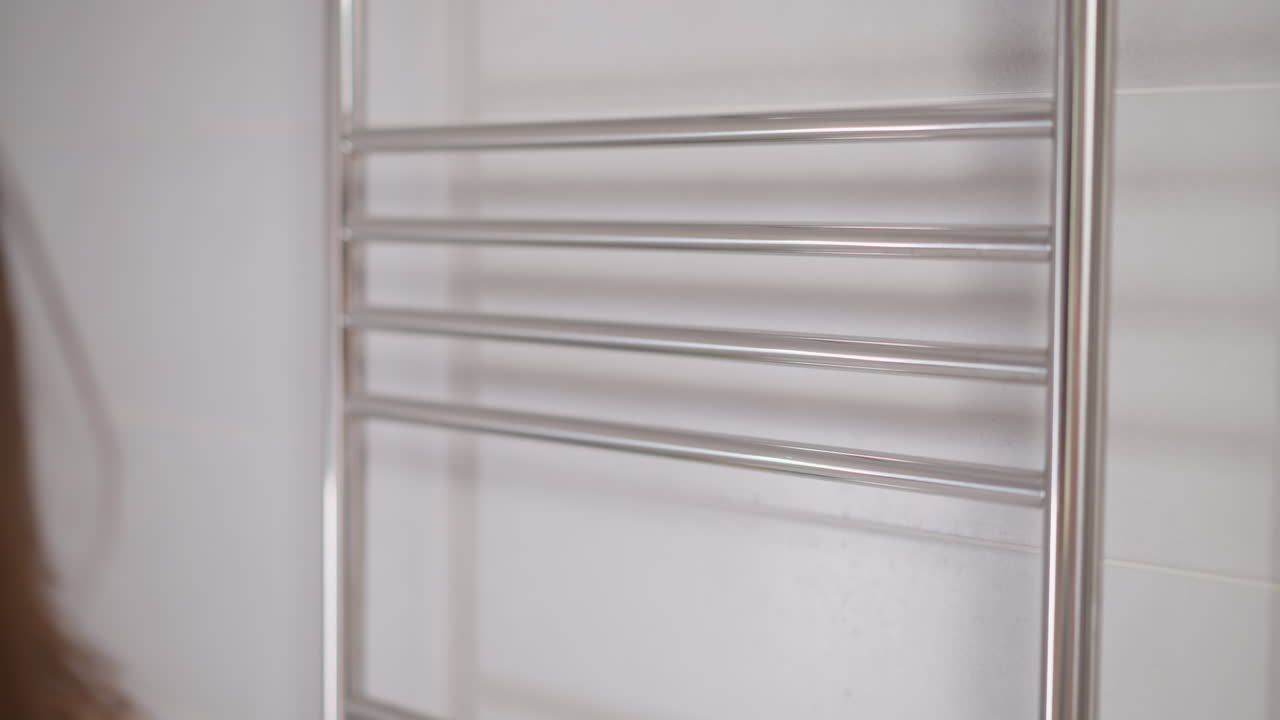 una mujer quita una toalla de terry suave de la percha en el baño en cámara lenta. una mujer morena toma una toala de terry con las manos para limpiar la cara después de los cosméticos