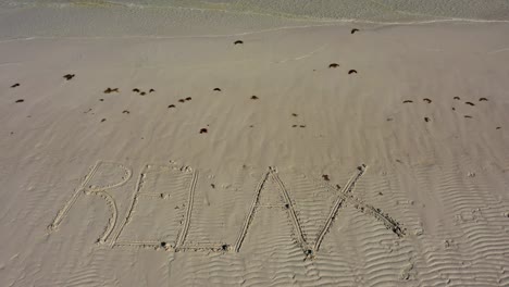 Relájese-Muy-Pequeño-En-El-Marco,-Inscrito-En-La-Arena-De-Una-Playa-Mientras-El-Agua-Cae-Sobre-La-Playa