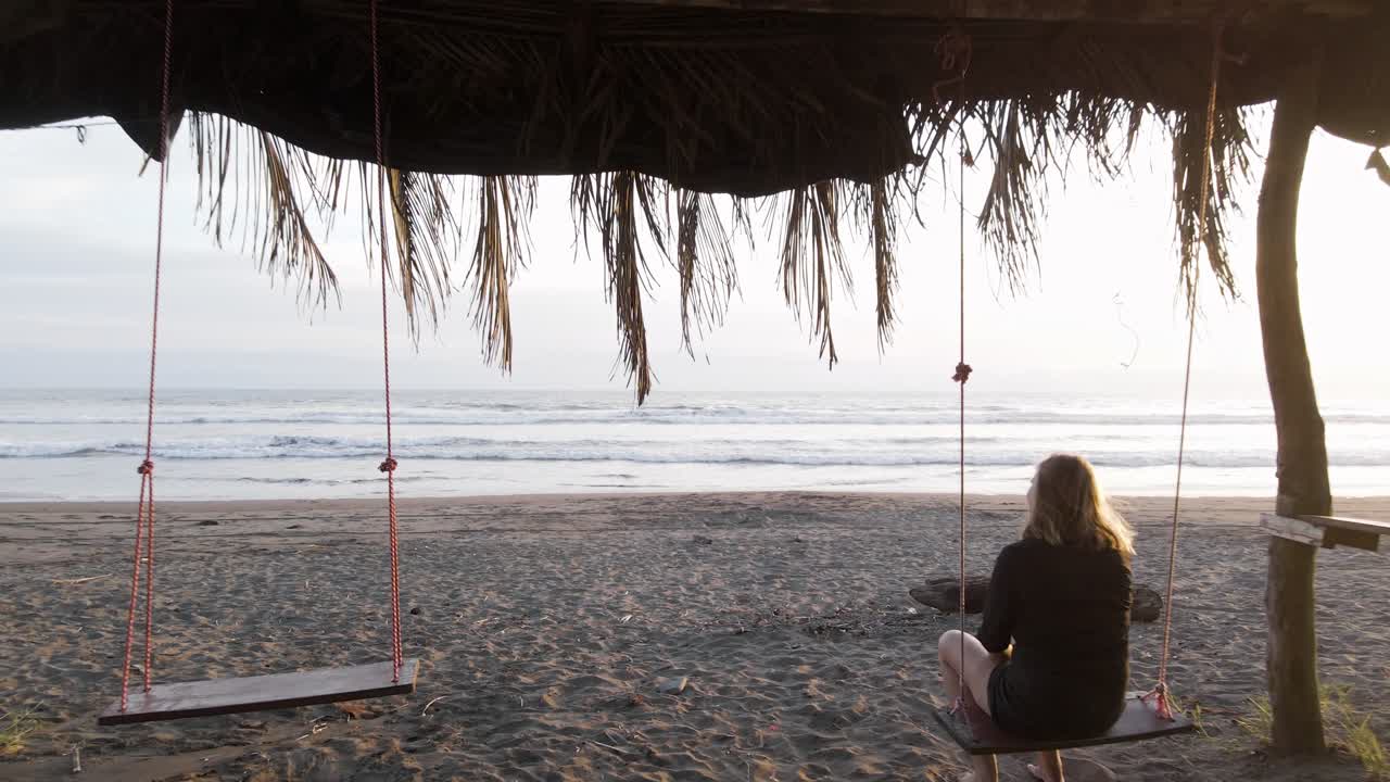 una joven rubia disfrutando de una hermosa puesta de sol mientras estaba sentada en un columpio en una playa de costa rica