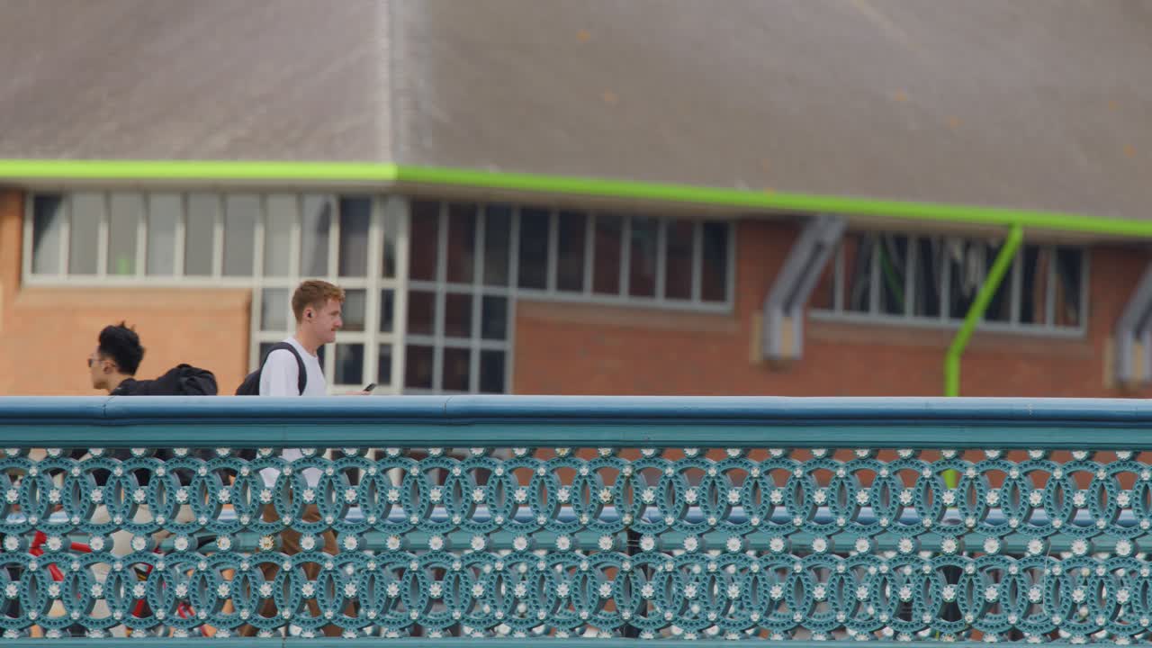 Two individuals walk and talk across ornate city bridge, daylight, steady side view camera