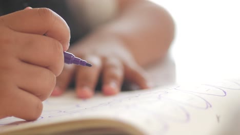 a child's hand drawing with a purple marker in a notebook