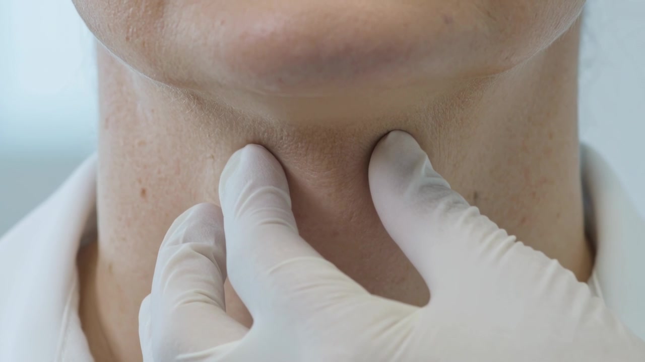 Entrando nell'inquadratura, medico guantato che posiziona le dita su una donna con colletto bianco in clinica, controllando la tiroide.