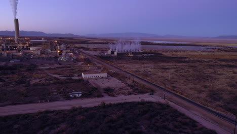 Power-generation-manufacturer-plant,-car-driving-on-rural-road-at-dusk,-aerial-forward