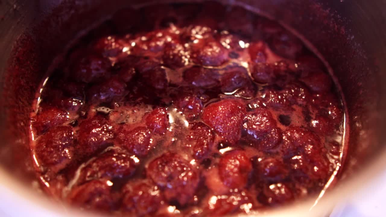 Bubbles slowly rising to the surface of hot strawberry jam cooking in a small saucepan, SLOMO