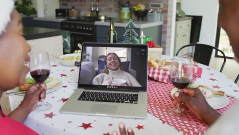 African-american-couple-with-wine-using-laptop-for-christmas-video-call-with-happy-woman-on-screen