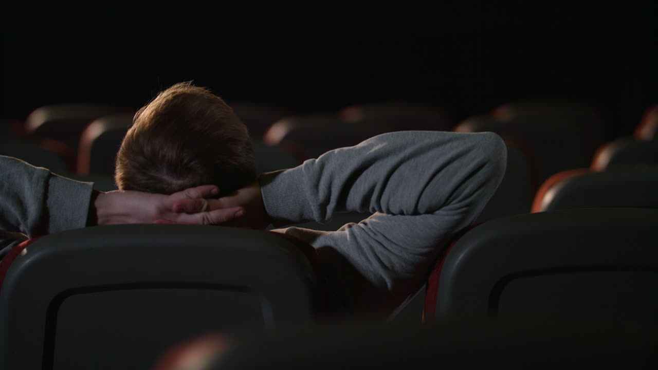 Young man relaxing in empty dark theatre