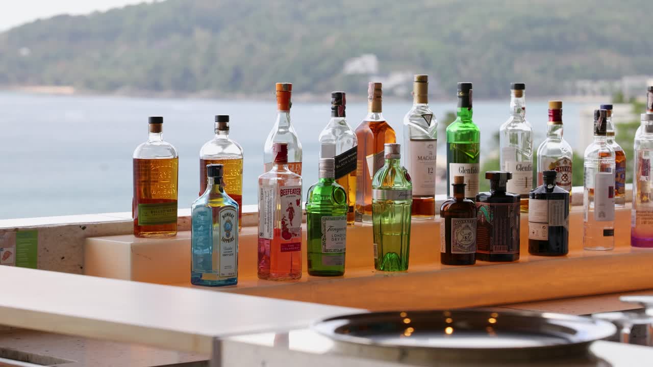una colección de botellas coloridas en un mostrador de bar con un paisajístico fondo oceánico en phuket, tailandia. iluminación natural brillante