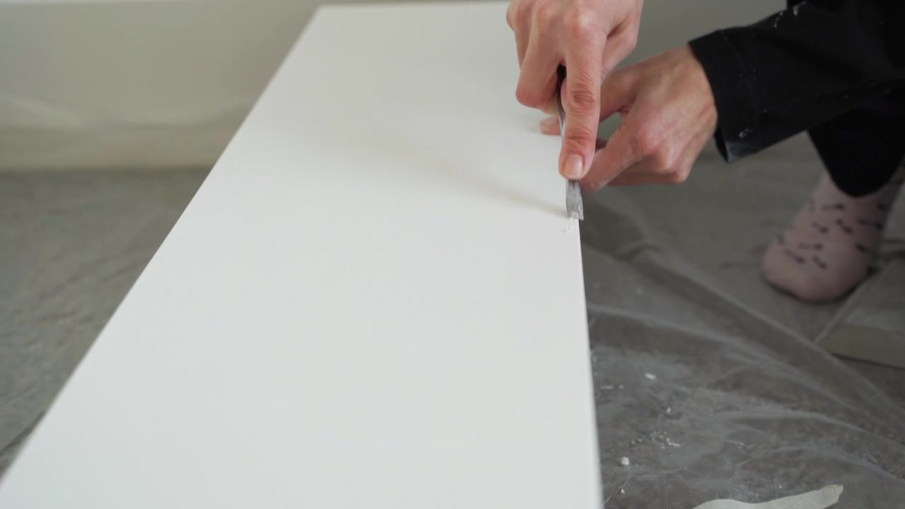 Girl removing paint burr from a white wooden board, dolly in shot.