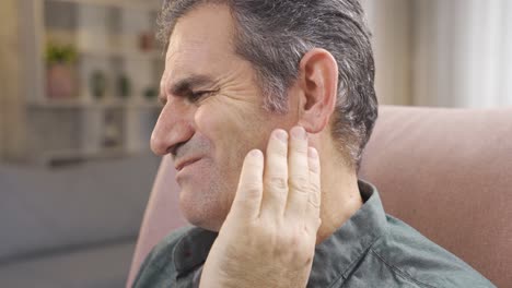 mature man with sore ears rubbing his ear with hands.