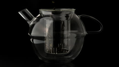 loose tea pouring into glass teapot