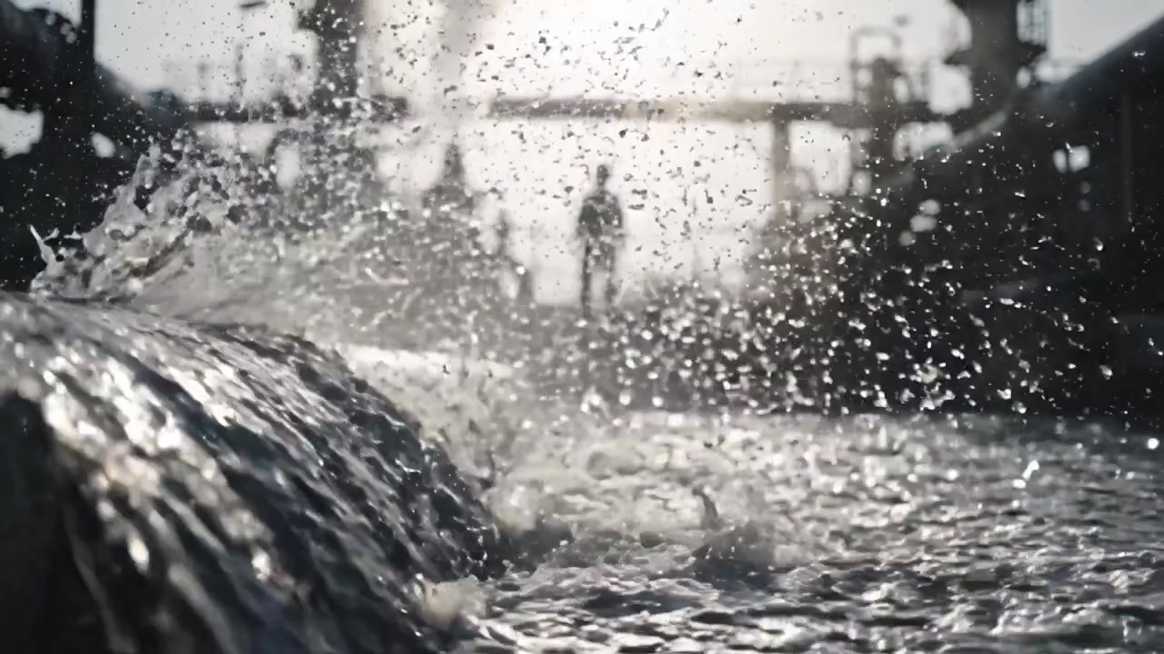De dynamische interactie van water en industrie vastleggen: Een close-up van stromend water te midden van industriële structuren en figuren op de achtergrond