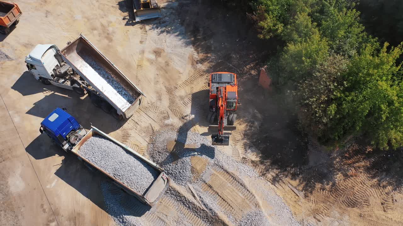 View from above on excavator and two trucks. Excavator working near the machinery with granite stones. Aerial view.