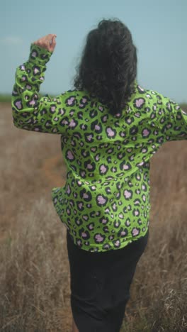person walking on dry grass trail in bold green leopard shirt, sunny day outdoors