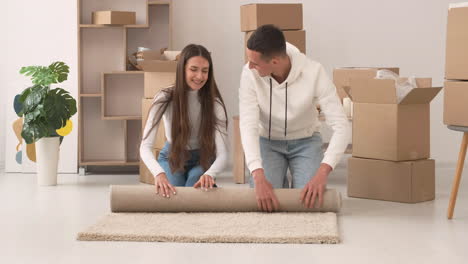 front view of a young couple in a new house sitting on the floor rolling a carpet