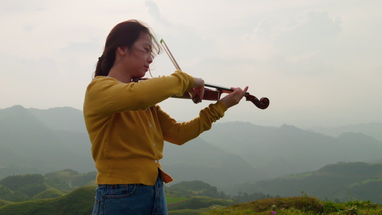 la mujer se centra atentamente en cada nota que viene de su violín perfectamente afinado mientras toca en la ladera de una montaña en este entorno fantástico