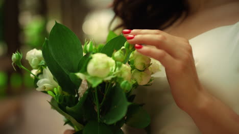 manos de la mujer tocando el ramo en el parque. la novia de pie con flores en el jardín