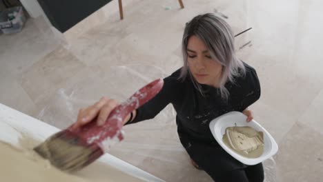 artista femenina sentada al lado del caballete con lienzo pintando algo en su estudio de arte - cámara lenta