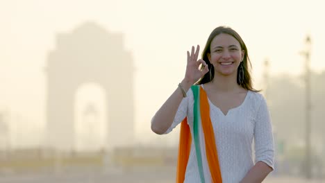 Happy-Indian-girl-showing-Okay-sign-at-India-gate-in-an-Indian-wear