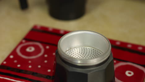 un primer plano de la parte inferior de una cafetera de espresso con una persona que agrega el filtro y el café
