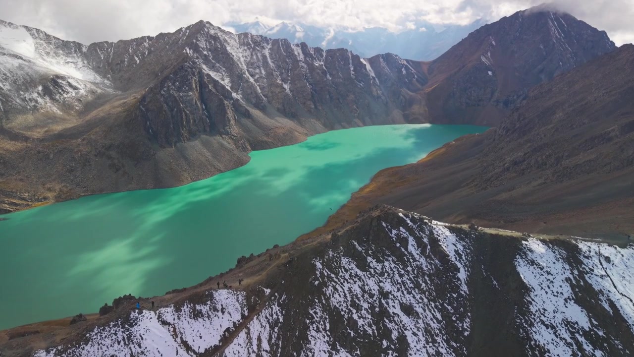 Karakol, Kırgızistan'da turkuaz renkli buzul gölü ve sarp zirvelerin üzerindeki karla kaplı Ala-Kul Geçidi sırtında yürüyüş yapan dağcıların yüksekten çekilmiş hava görüntüsü