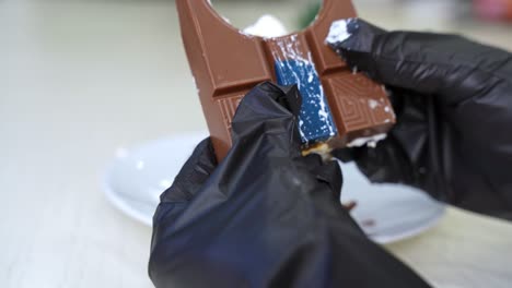 close-up of gloved hands holding bitten chocolate bar—ideal for dessert, food styling, or hygiene-related visuals.