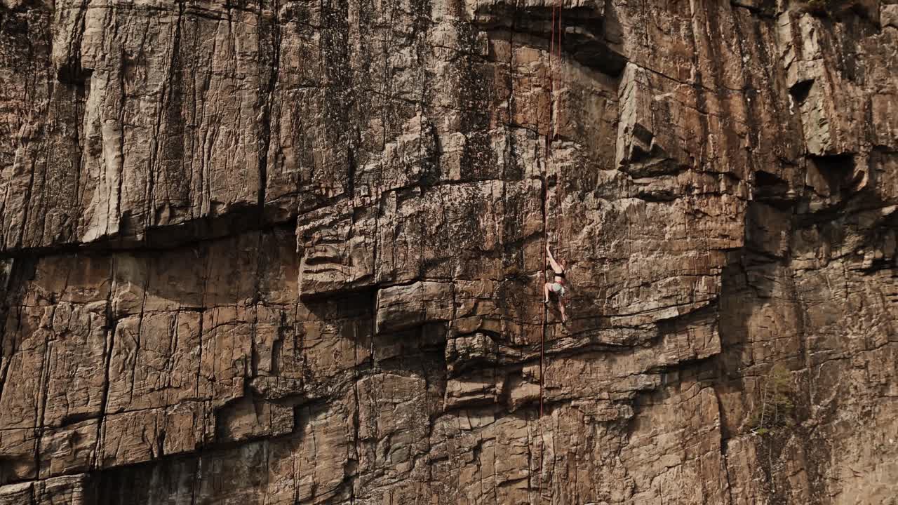 mujer poderosa escalando una pared de roca extremadamente peligrosa, vista aérea