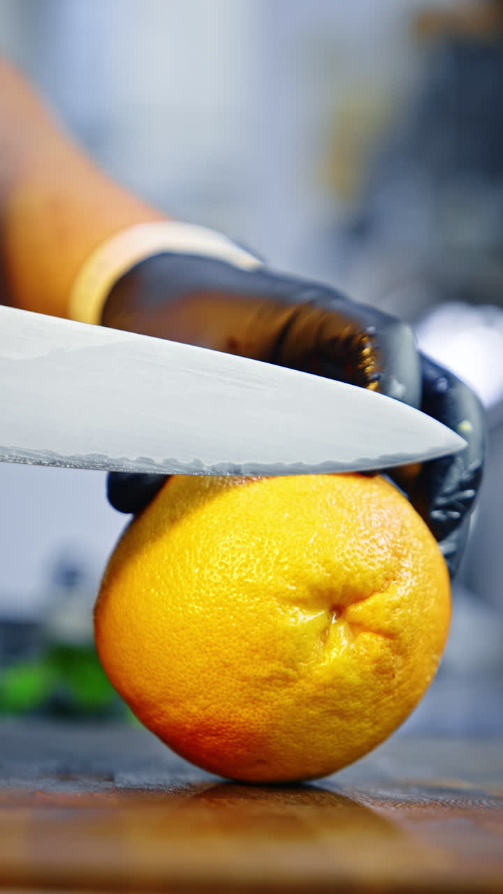 Hands wearing black latex gloves gut the peel of a grapefruit. Close up. Blurred backdrop. Vertical video.