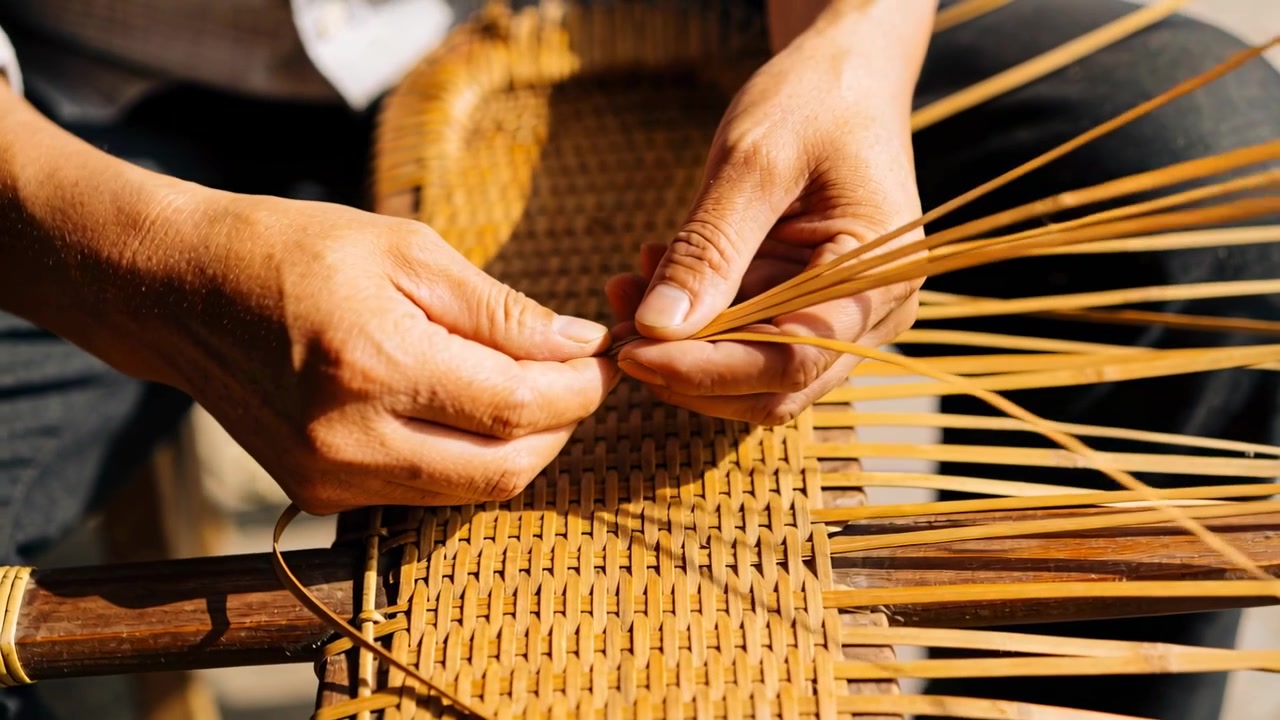 Mani artigiane in maglietta che raccolgono canne, allineando strisce da tessere su un telaio di legno per finire un pannello intrecciato.