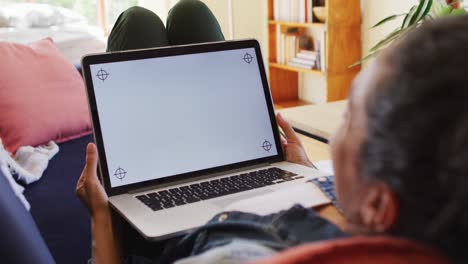 mujer caucásica usando una computadora portátil en una videollamada, acostada en el sofá en casa