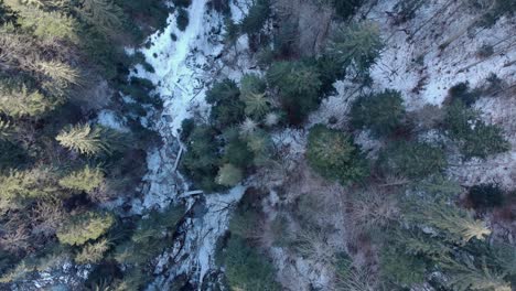 Above-View-Of-High-Forest-Mountains-With-Frozen-Stream-In-Winter