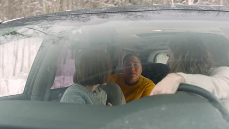 three friends talking together while sitting in the car on a winter day