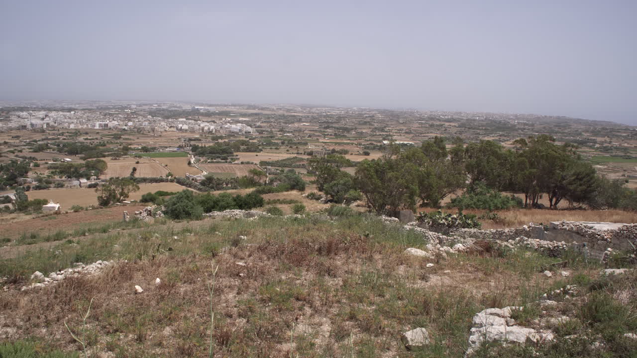 Paesaggio rurale 4K con il Mar Mediterraneo e una piccola città in lontananza sull'isola di Malta durante una calda giornata estiva