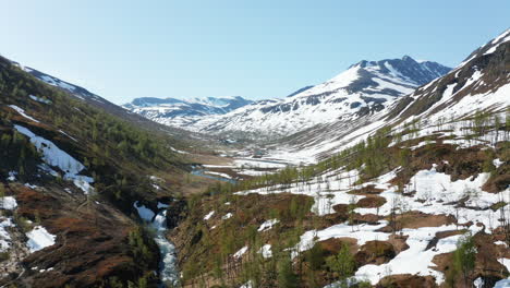 aerial, tracking drone shot overlooking the top of mohcuhatgaisa, in middle of snowy mountain peaks , blue sky, on a bright, sunny, summer day, in the lyngen alps, north norway