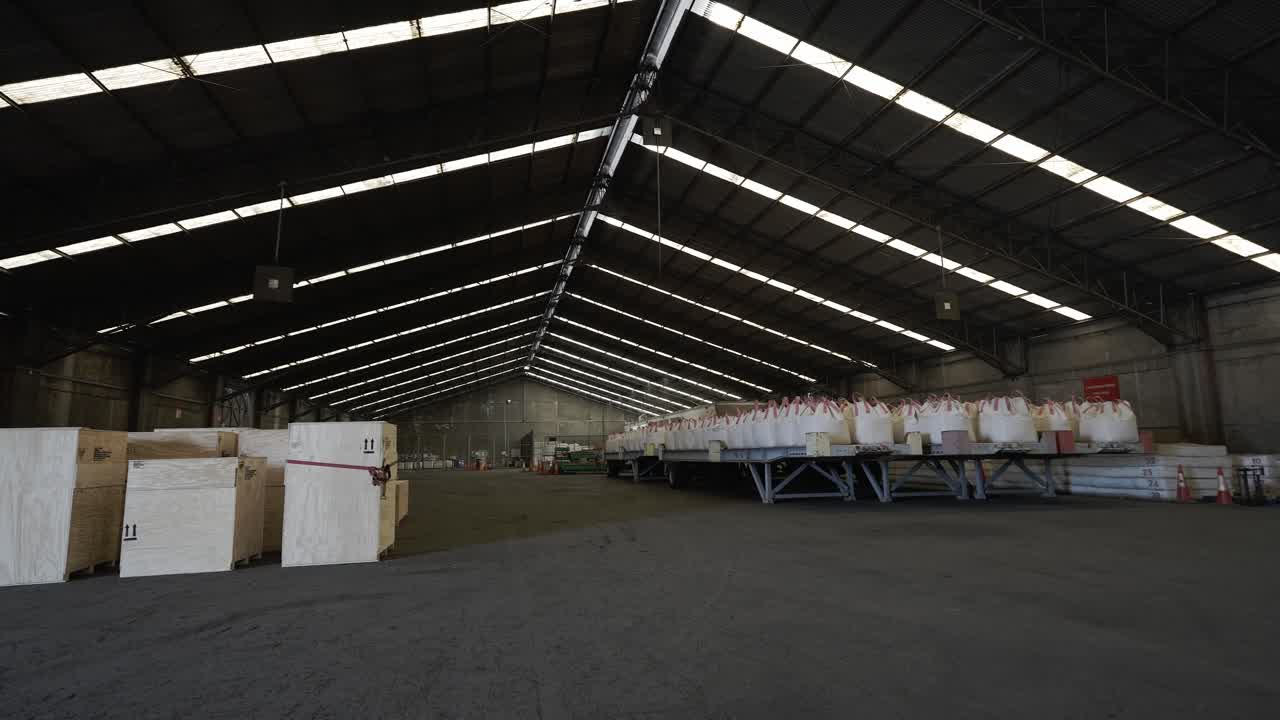L'area di stoccaggio mostra un grande magazzino con molte scatole imballate allineate su pallet. Luci intense dall'alto illuminano mentre gli operai preparano gli articoli per la consegna