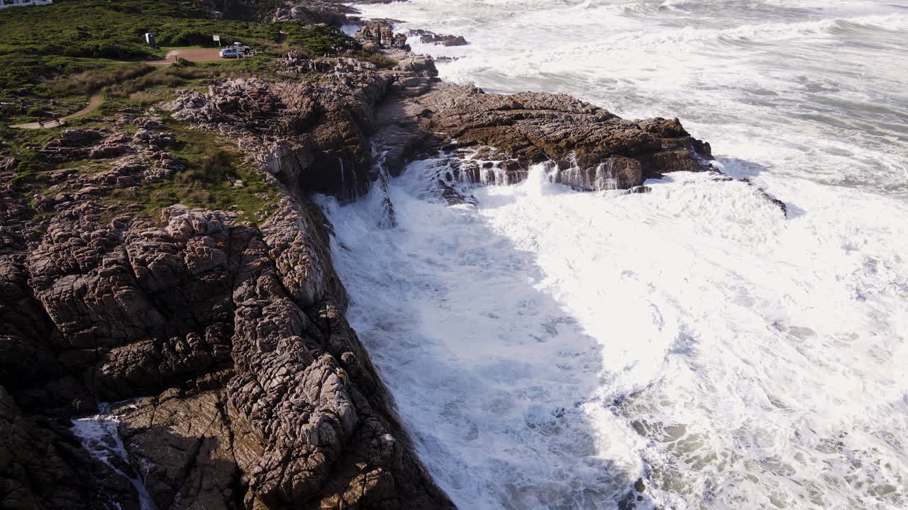 drone pullback tilt-up sobre el agua de mar espumosa surgiendo contra las rocas, hermanus