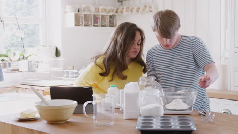 Una-Pareja-Joven-Con-Síndrome-De-Down-Sigue-Una-Receta-En-Una-Tableta-Digital-Para-Hornear-Pasteles-En-La-Cocina-De-Casa