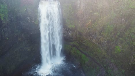 Fast-Rushing-Waterfall-with-Path-Behind-Leading-to-Cave-in-Wales-UK---Aerial-Drone-shot-4K