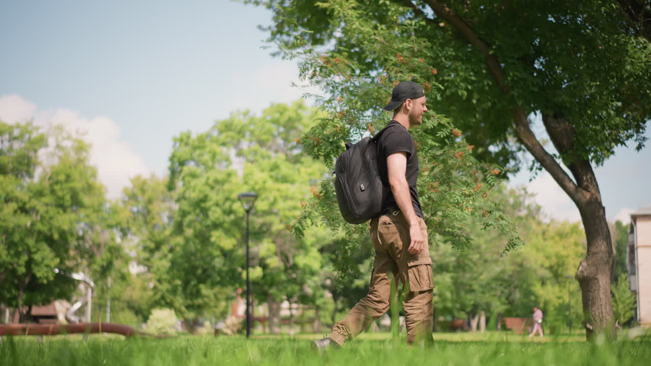 Solo Male Strolling Through Sunlit Park, Casual Male Artist Contemplating Amidst Lush Green Surroundings, Independent Male Creator Taking Peaceful Walk Under Shaded Trees During Sunny Summer Day