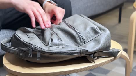 close-up of a person holding a black power bank above a grey backpack on a table. modern tech gear scene in a cozy home interior. perfect for tech, travel, or lifestyle themes.