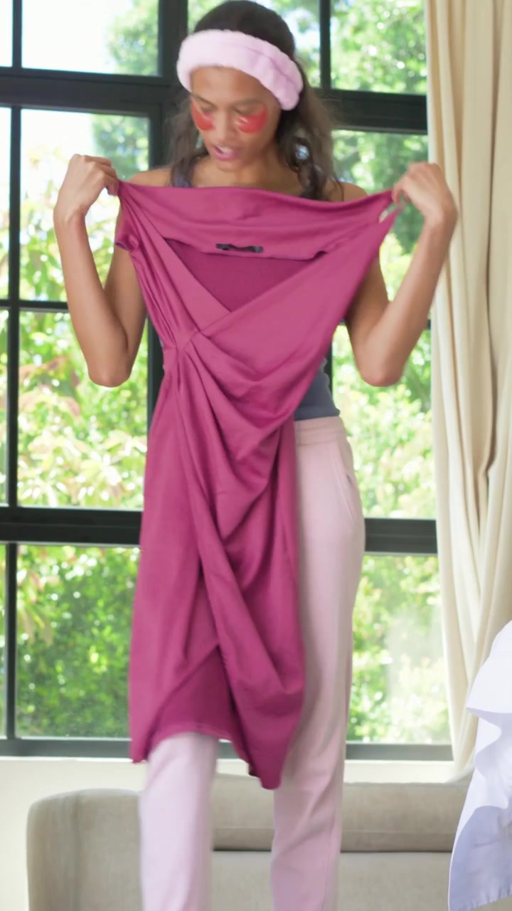 Vídeo vertical: Selecionando vestido magenta, mulher de regata e calça verificando as alças e estendendo-o na cama.
