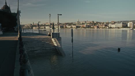 flooded riverbank steps leading into the danube river in budapest under clear skies near the parliament building