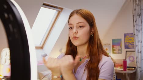 teen girl applying makeup in bedroom